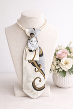 Load image into Gallery viewer, necklace with necktie on jewelry bust with flowers in the vase in the background
